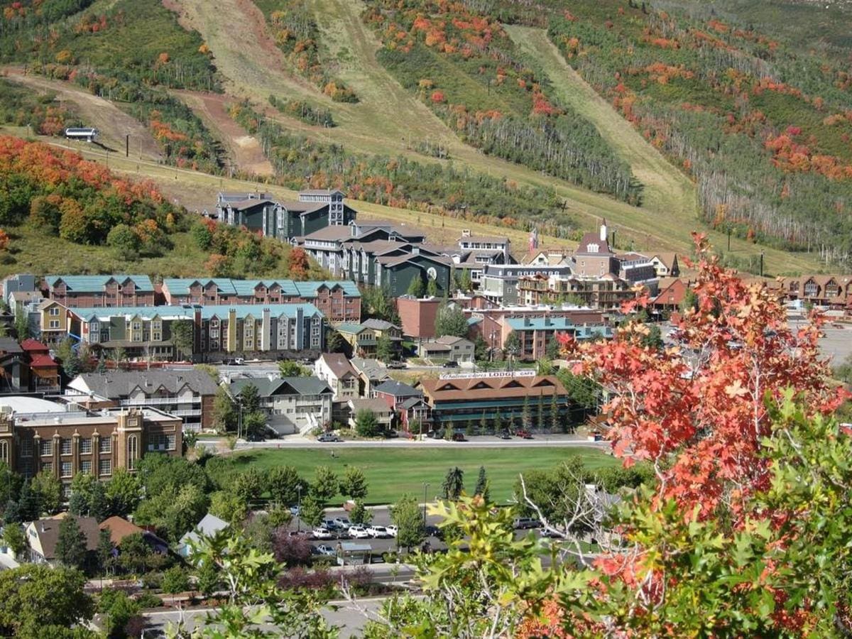 A scenic view of a town nestled in a valley with buildings surrounded by autumnal trees and hills in the background.