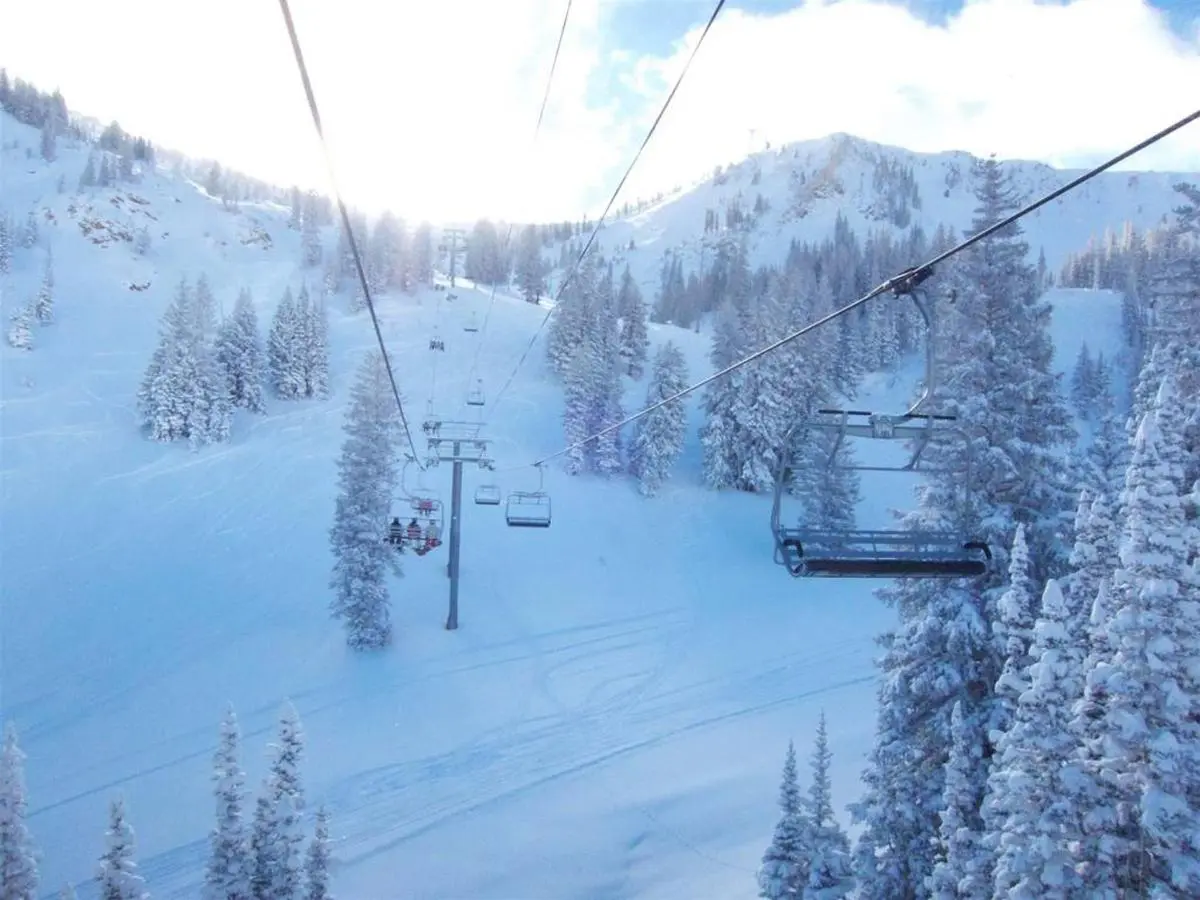 A ski lift gracefully ascends the snowy mountain, flanked by pine trees under a bright sky—a perfect scene for those enjoying Park City ski vacation rentals.