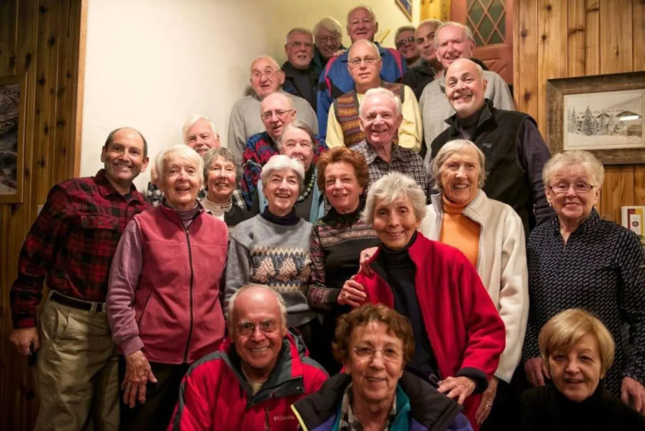 A group of older adults pose for a photo on a staircase indoors, all smiling at the camera, enjoying their time together during a trip made possible by the free bus route.