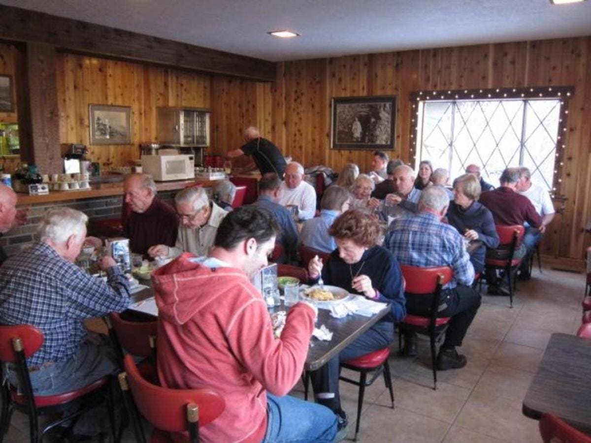 A group of people enjoying a meal at a cozy restaurant with wooden walls and red chairs, conveniently located near the free bus route for easy access to local lodging options.