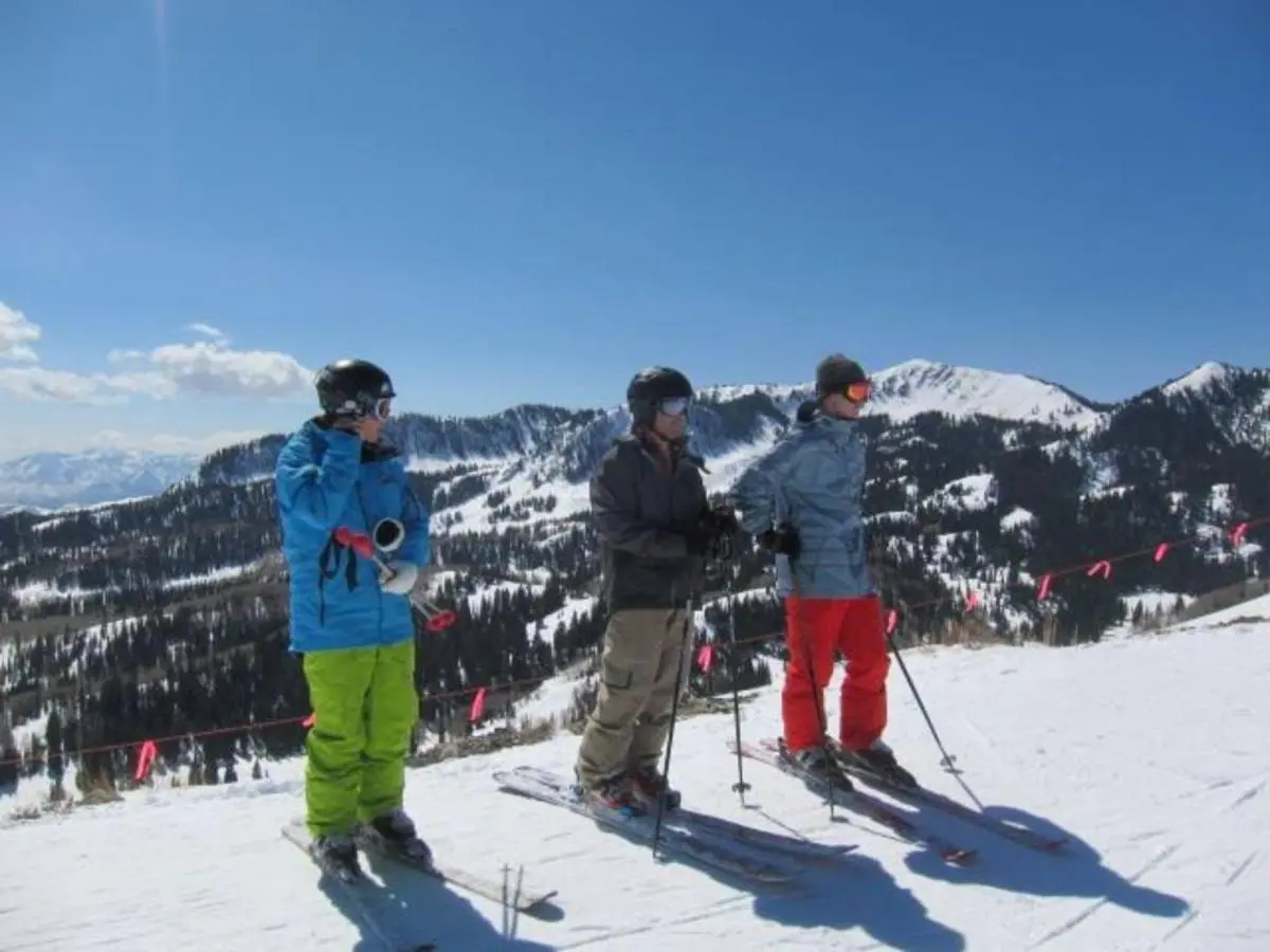 Three skiers in colorful gear stand on a snowy slope, overlooking a mountainous landscape under a clear blue sky. Nearby, family-friendly lodging in Park City offers the perfect retreat after a day of adventure.