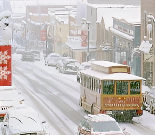 A city street, lined with snow-dusted cars and a trolley gliding through, showcases buildings on both sides. In this winter wonderland, private room rentals offer cozy retreats just steps away from the snowy bustle.