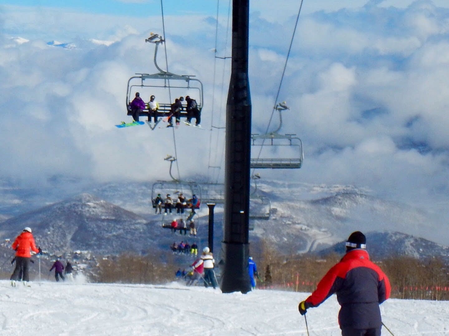 Skiers on a snowy slope ride a chairlift under a mostly cloudy sky, enjoying the breathtaking views offered by Park City Ski Vacation Rentals.