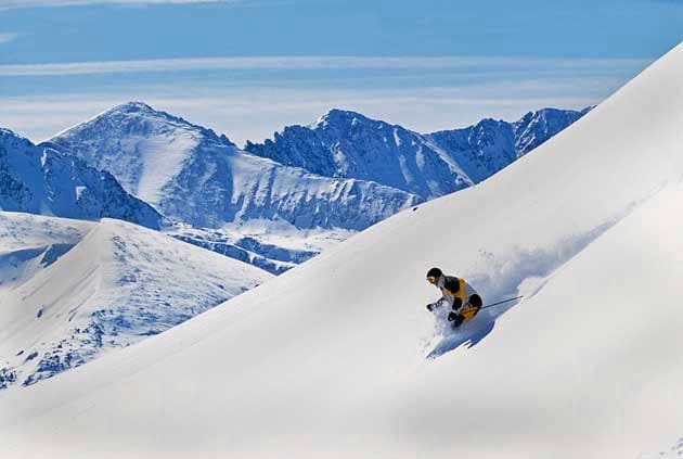 A person skiing down a snow-covered mountain slope with distant snow-capped peaks in the background, reminiscent of a thrilling Park City ski vacation.