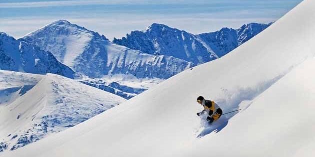 A person skiing down a snow-covered mountain slope with distant snow-capped peaks in the background, reminiscent of a thrilling Park City ski vacation.